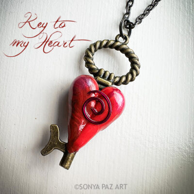 Red heart-shaped key pendant on a chain with a twisted bronze ring; caption 'Key to my Heart' visible.