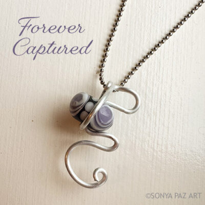 Handcrafted silver wire pendant with lilac marbled beads on a chain, beside the purple script text 'Forever Captured'