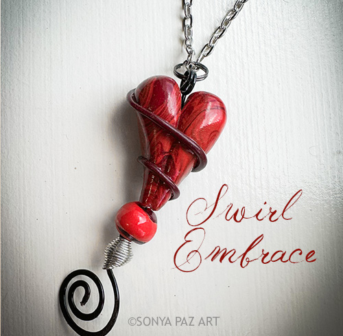 Red heart pendant wrapped in wire on a silver chain, with the script 'Swirl Embrace' beside it.