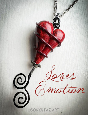 Red heart pendant wrapped in silver wire, hanging from a chain, with the text 'Loves Emotion' beside it.