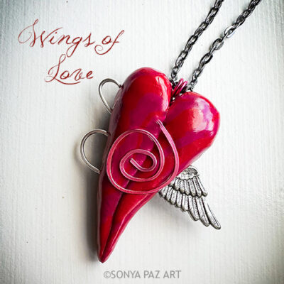 Pink heart pendant in the shape of a winged heart on a chain, with 'Wings of Love' text above left.